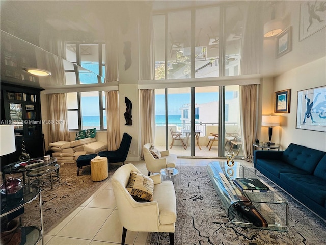 living room with a towering ceiling, a water view, and tile patterned floors