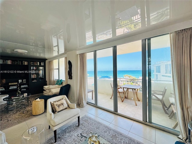 living area with tile patterned floors, a water view, and a beach view