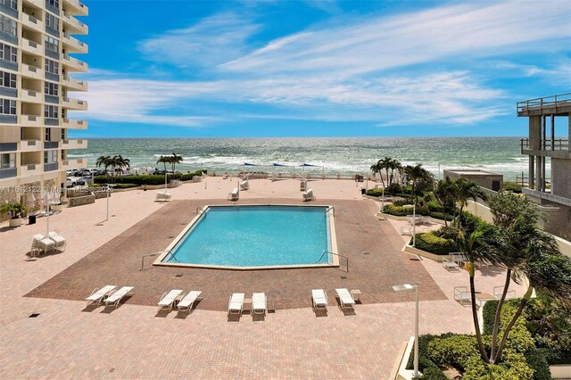 view of swimming pool with a patio area, a water view, and a view of the beach