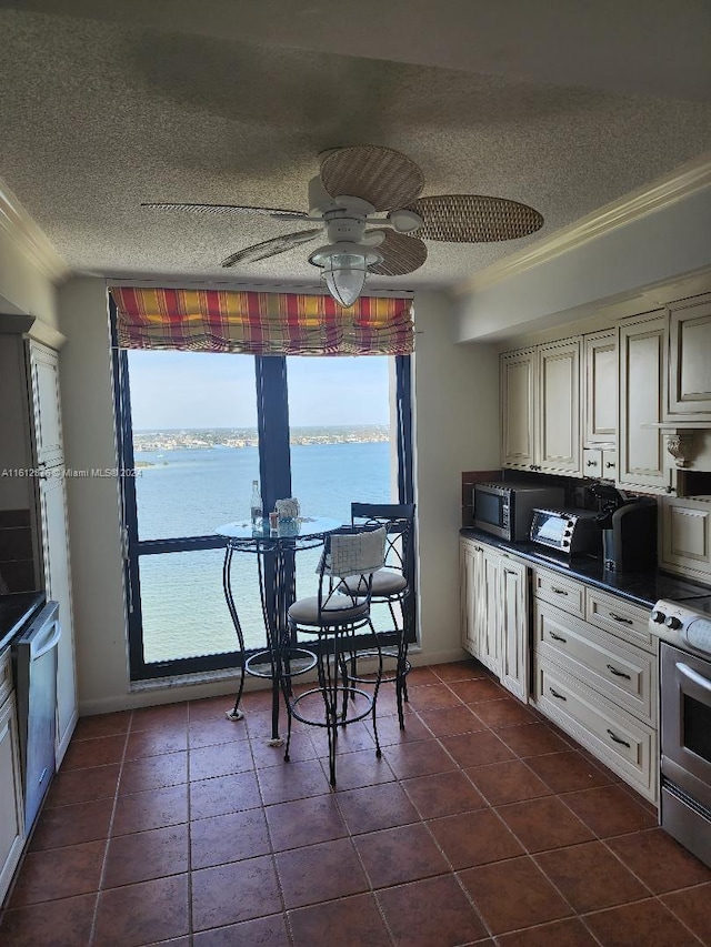 kitchen featuring stove, dark tile patterned floors, a water view, ceiling fan, and ornamental molding