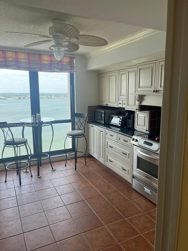 kitchen with stove, a water view, ceiling fan, and dark tile patterned floors