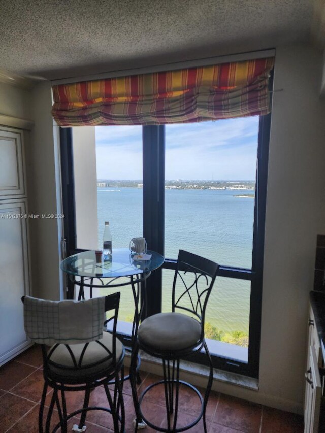 dining space featuring a water view, a textured ceiling, and dark tile patterned flooring