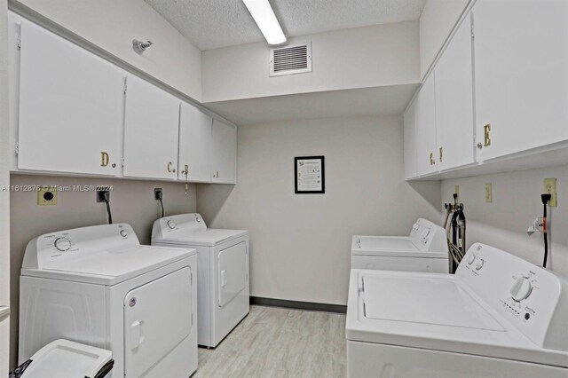 clothes washing area featuring washing machine and clothes dryer, light wood-type flooring, cabinets, and a textured ceiling