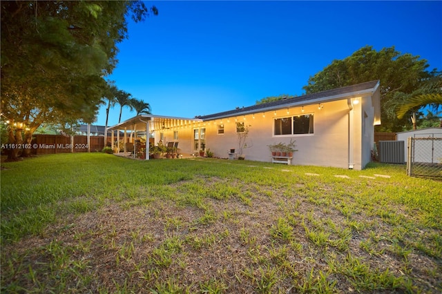 rear view of property featuring a lawn and central air condition unit