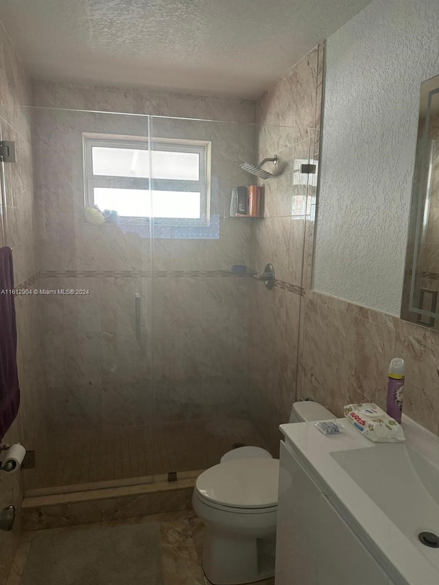 full bath with a textured wall, toilet, a stall shower, a textured ceiling, and vanity