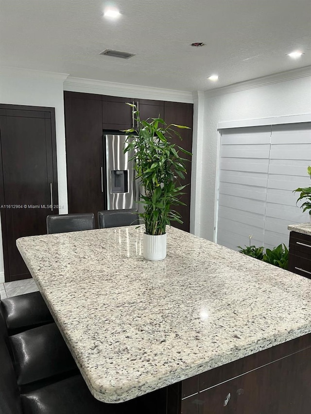 kitchen with light stone counters, a center island, stainless steel fridge, a kitchen bar, and crown molding