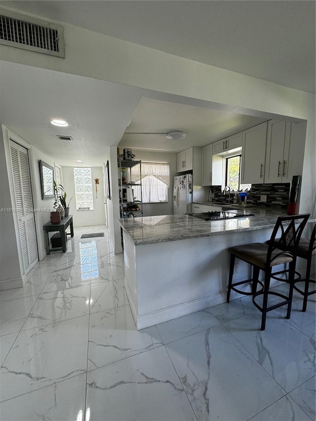 kitchen featuring stainless steel fridge with ice dispenser, kitchen peninsula, tasteful backsplash, light tile floors, and a breakfast bar