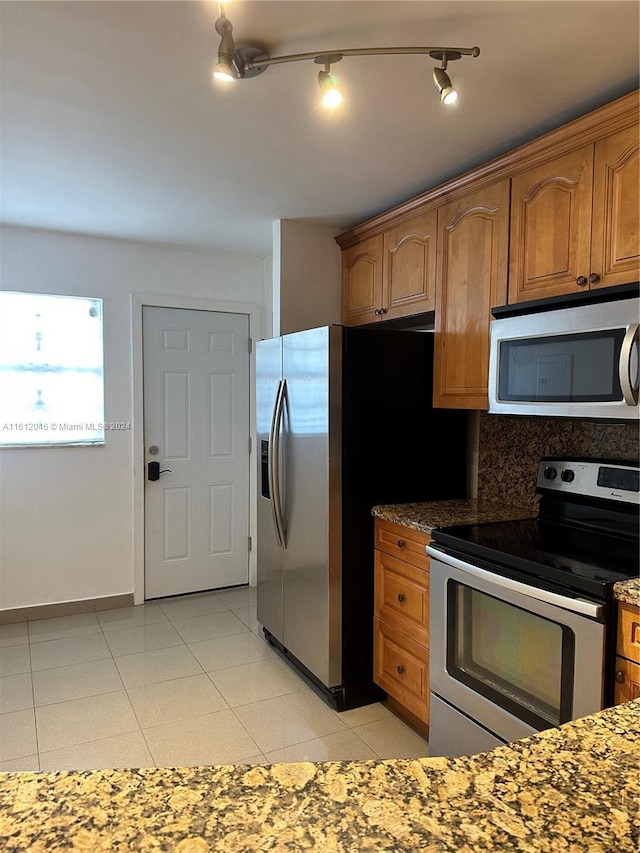 kitchen featuring decorative backsplash, appliances with stainless steel finishes, light tile patterned floors, and dark stone countertops