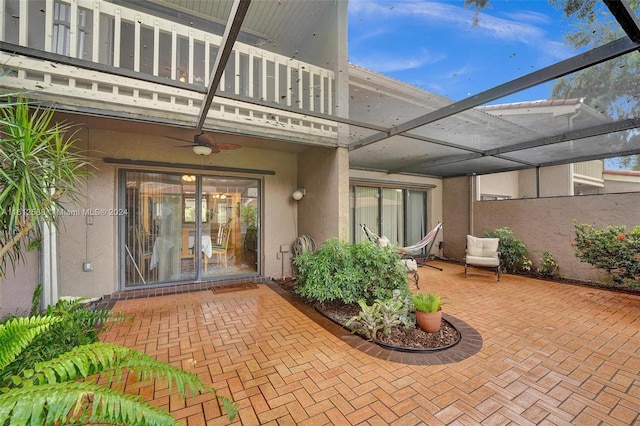 view of exterior entry with ceiling fan, a balcony, and a patio