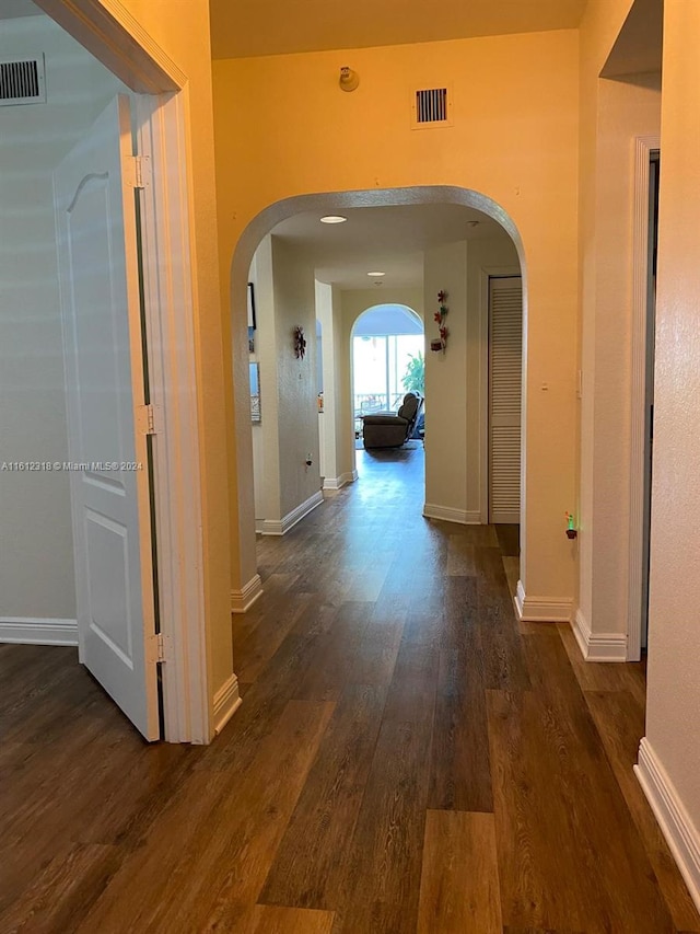 corridor with dark wood-style floors, arched walkways, visible vents, and baseboards