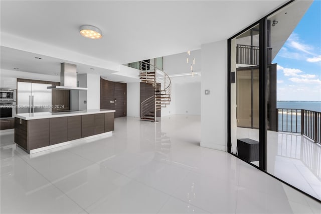 kitchen featuring island exhaust hood, dark brown cabinets, light tile patterned floors, a water view, and a center island