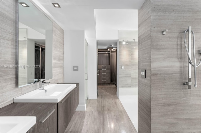 bathroom featuring a shower with door, vanity, wood-type flooring, and tile walls