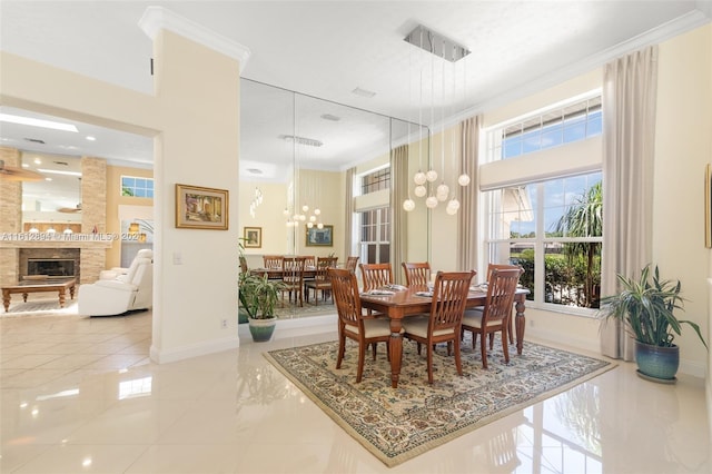 tiled dining area with a towering ceiling, a stone fireplace, a chandelier, and crown molding