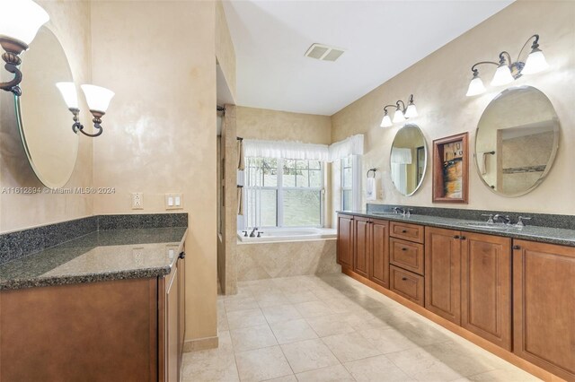 bathroom with tile flooring, a relaxing tiled bath, and dual bowl vanity