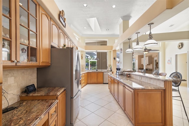 kitchen with stainless steel appliances, pendant lighting, dark stone countertops, light tile floors, and a breakfast bar area