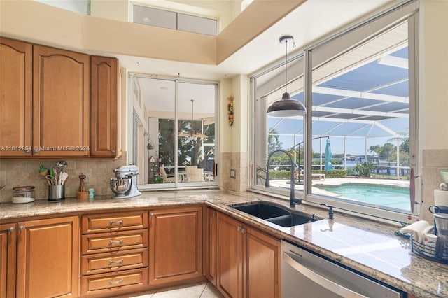 kitchen featuring hanging light fixtures, stainless steel dishwasher, light stone counters, backsplash, and sink