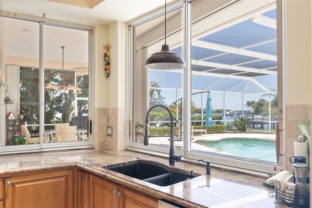 interior space with light stone counters, hanging light fixtures, sink, and backsplash