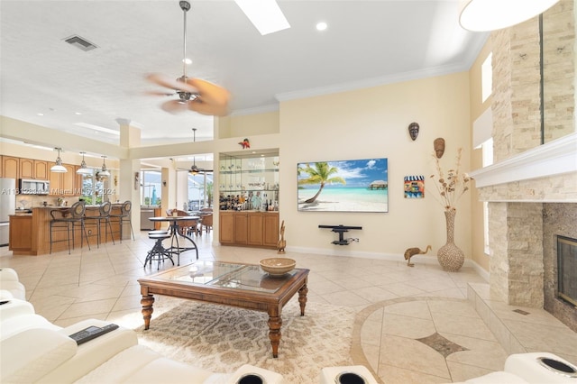 tiled living room featuring a fireplace, a skylight, a high ceiling, ornamental molding, and ceiling fan