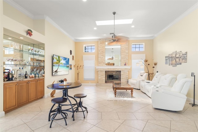 tiled living room featuring a stone fireplace, ceiling fan, a skylight, and ornamental molding