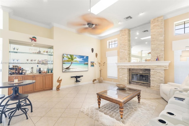 living room with ornamental molding, a high ceiling, a stone fireplace, ceiling fan, and light tile floors