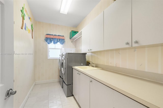 laundry room featuring washing machine and clothes dryer, light tile floors, wooden walls, sink, and cabinets