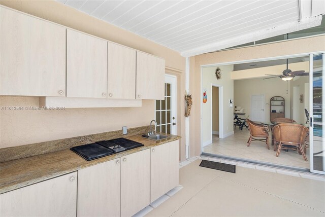 kitchen featuring light stone countertops, ceiling fan, black electric cooktop, light tile flooring, and sink