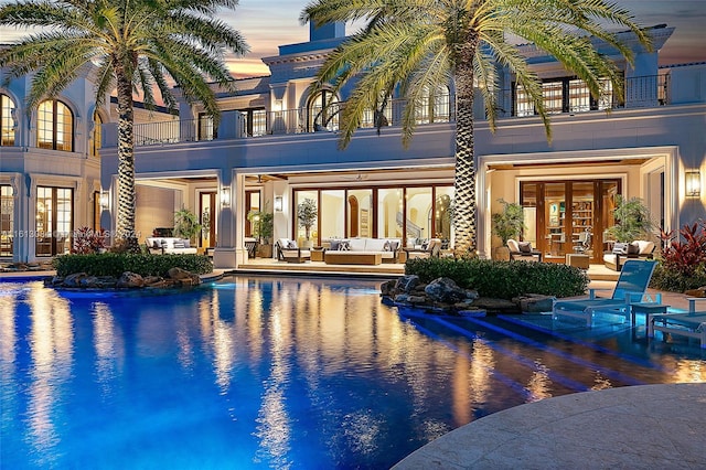 pool at dusk with outdoor lounge area, french doors, and a patio