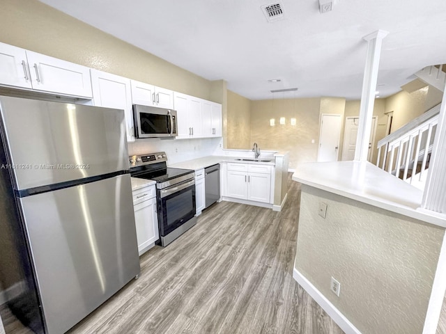 kitchen featuring stainless steel appliances, sink, decorative light fixtures, light hardwood / wood-style floors, and white cabinetry