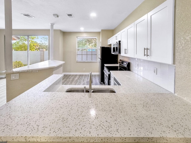 kitchen with kitchen peninsula, appliances with stainless steel finishes, white cabinets, and light stone counters