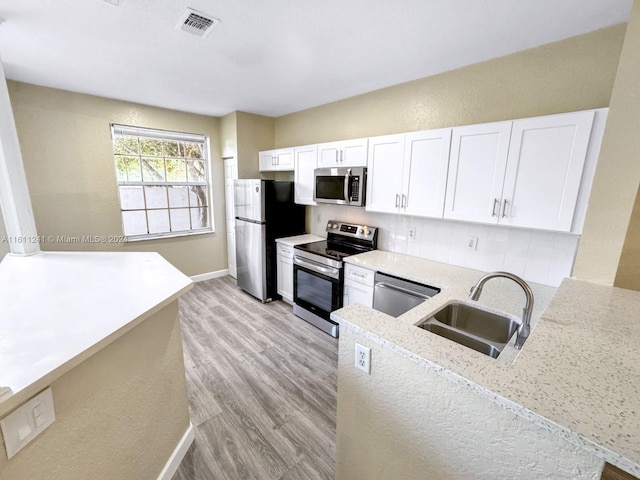 kitchen featuring appliances with stainless steel finishes, backsplash, light stone counters, sink, and white cabinetry