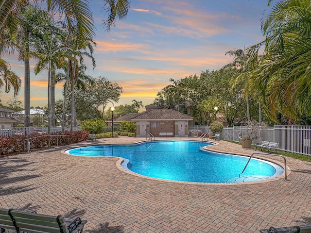 pool at dusk featuring a patio area and an outdoor structure