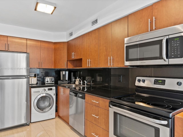 kitchen with brown cabinets, stainless steel appliances, dark countertops, a sink, and washer / dryer
