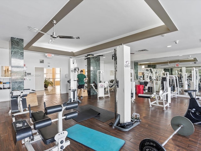 gym featuring a tray ceiling, wood finished floors, visible vents, and a ceiling fan