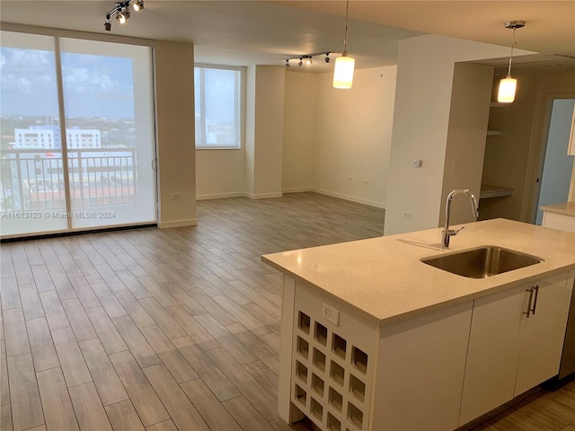 kitchen featuring sink, light hardwood / wood-style flooring, a kitchen island with sink, hanging light fixtures, and white cabinets