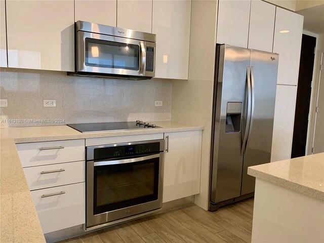 kitchen with light wood-type flooring, light stone counters, backsplash, white cabinetry, and appliances with stainless steel finishes