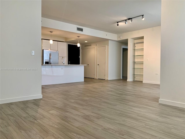 unfurnished living room featuring track lighting, sink, and light hardwood / wood-style floors