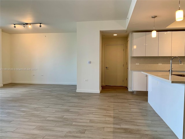 kitchen featuring backsplash, hanging light fixtures, white cabinetry, and light wood-type flooring