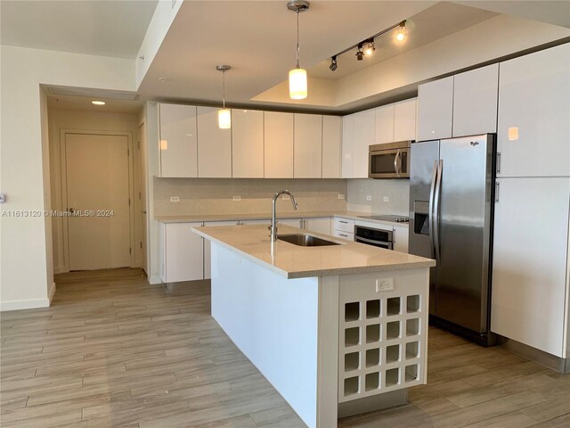 kitchen featuring stainless steel appliances, backsplash, sink, a kitchen island with sink, and white cabinetry