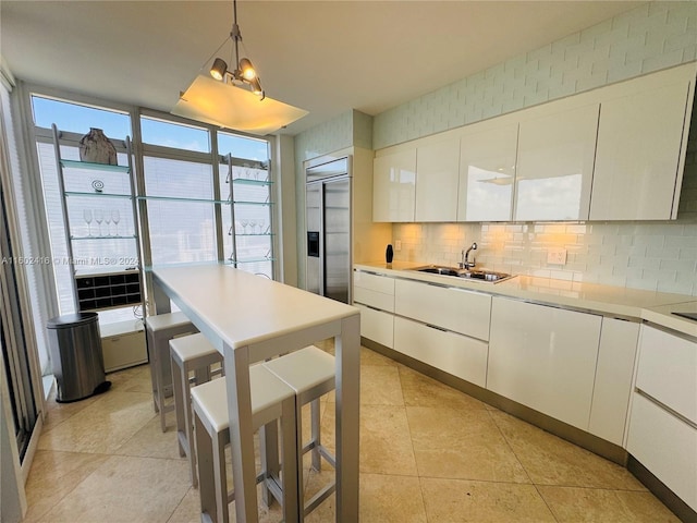 kitchen featuring tasteful backsplash, light countertops, built in fridge, a sink, and white cabinetry