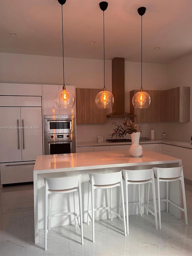 kitchen featuring pendant lighting, wall chimney exhaust hood, a breakfast bar area, and paneled built in refrigerator