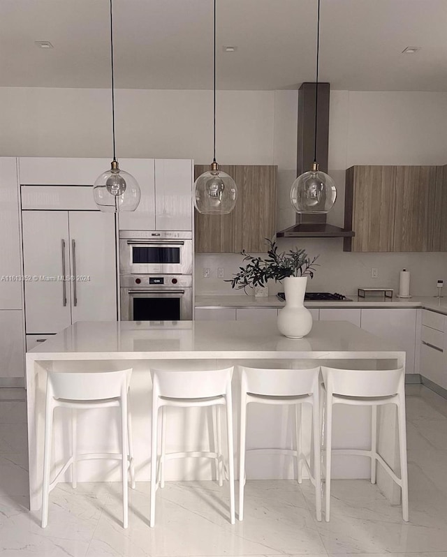 kitchen featuring double oven, light tile flooring, wall chimney exhaust hood, white cabinets, and a breakfast bar