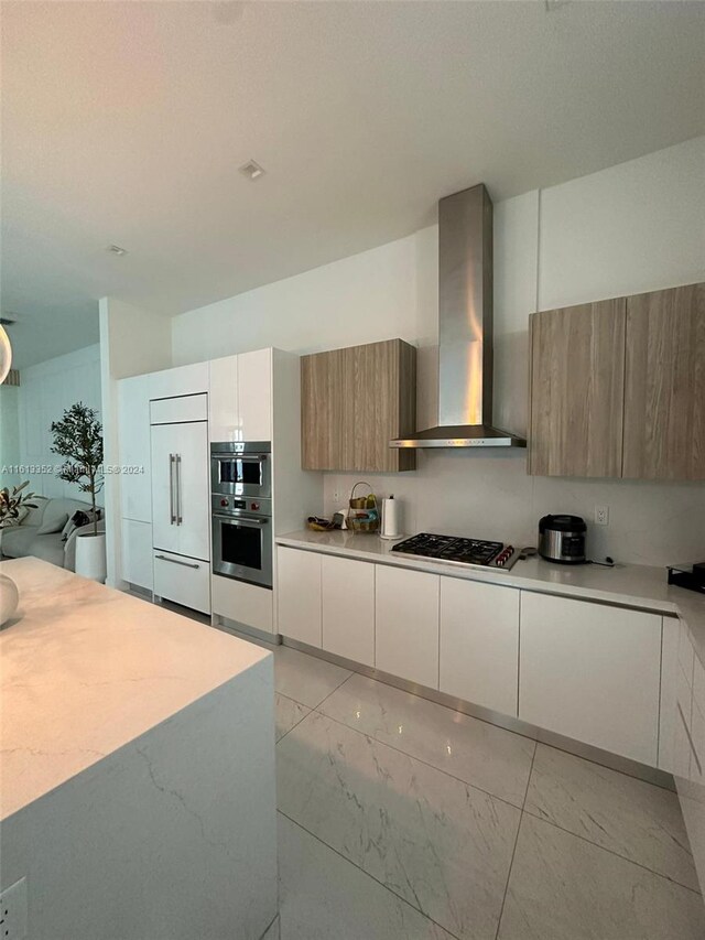 kitchen featuring stainless steel appliances, wall chimney range hood, light tile floors, and white cabinets