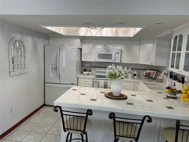 kitchen with white appliances, sink, tile countertops, white cabinets, and a breakfast bar area