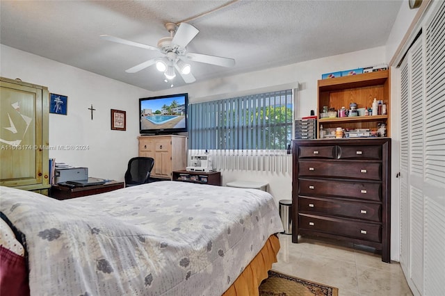 bedroom featuring light tile patterned floors, a ceiling fan, a closet, and a textured ceiling