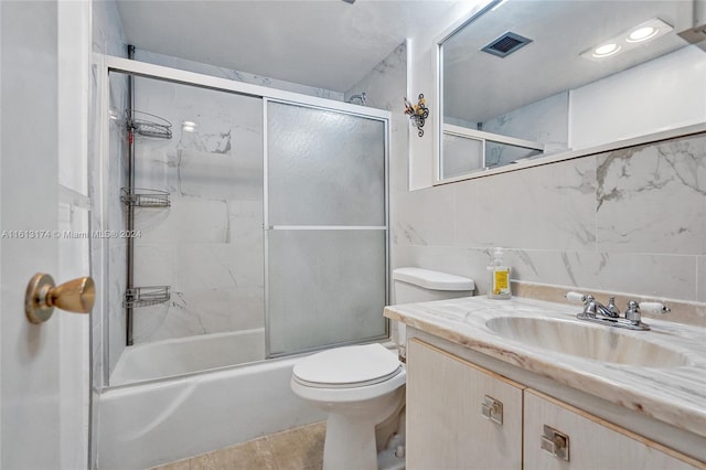 full bathroom featuring vanity, visible vents, shower / bath combination with glass door, tile walls, and toilet