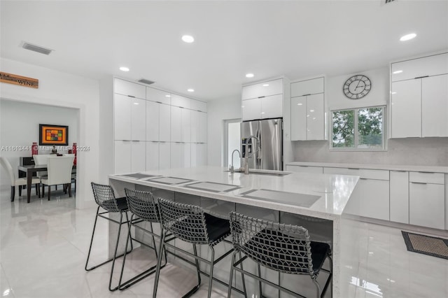 kitchen featuring white cabinetry, stainless steel fridge, a breakfast bar, and a kitchen island with sink