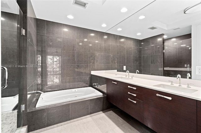 bathroom with a relaxing tiled bath, dual bowl vanity, tile flooring, and tile walls