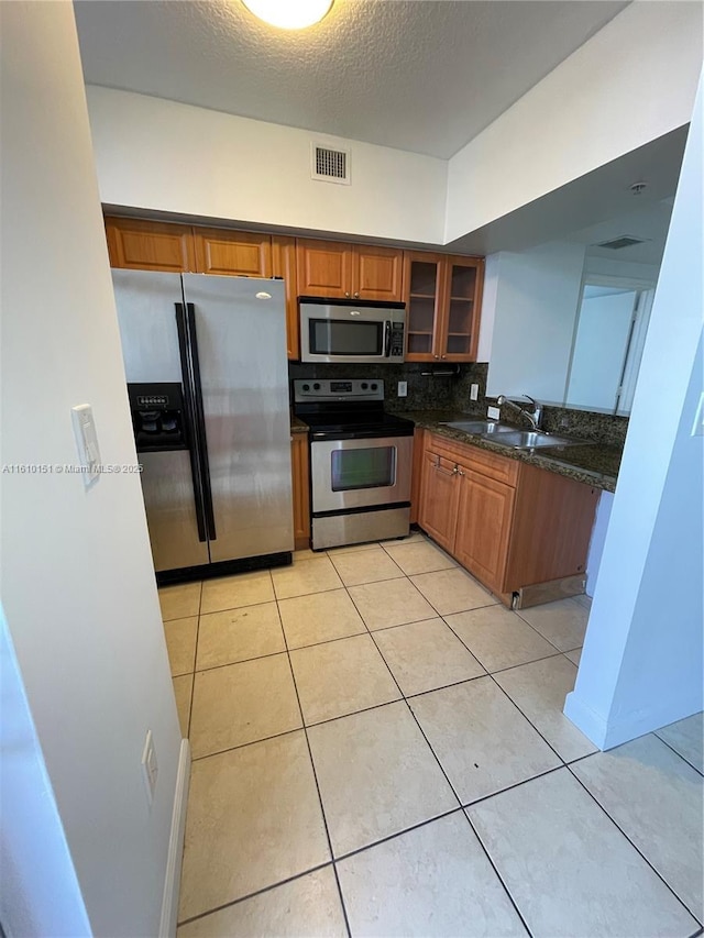 kitchen featuring sink, light tile patterned floors, dark stone countertops, stainless steel appliances, and decorative backsplash