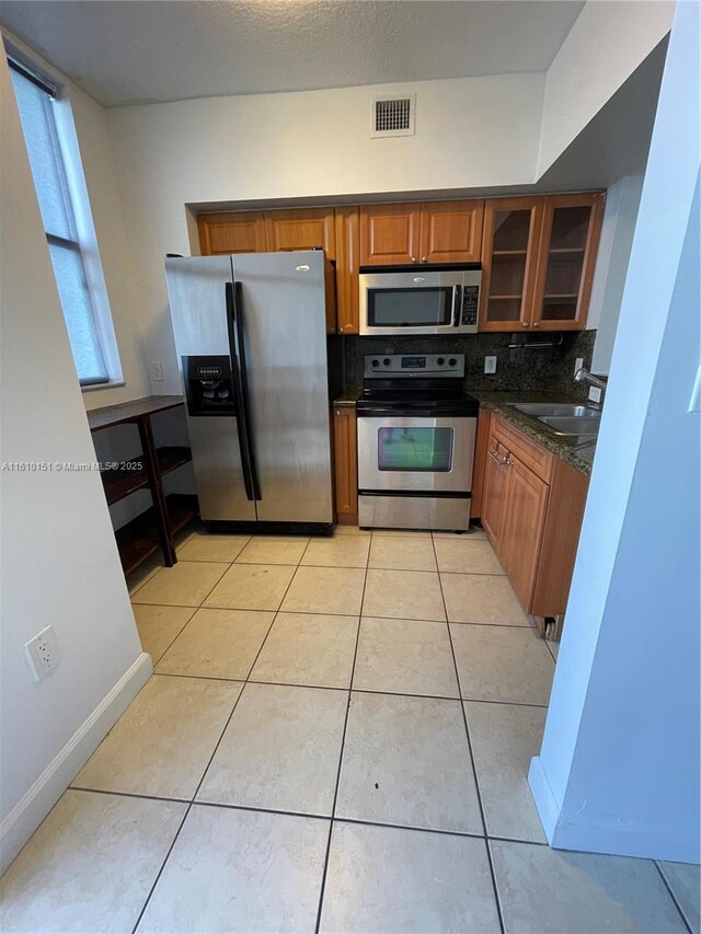 kitchen with sink, light tile patterned floors, stainless steel appliances, tasteful backsplash, and dark stone counters