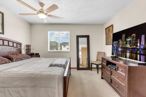 bedroom with light colored carpet, ceiling fan, and a textured ceiling